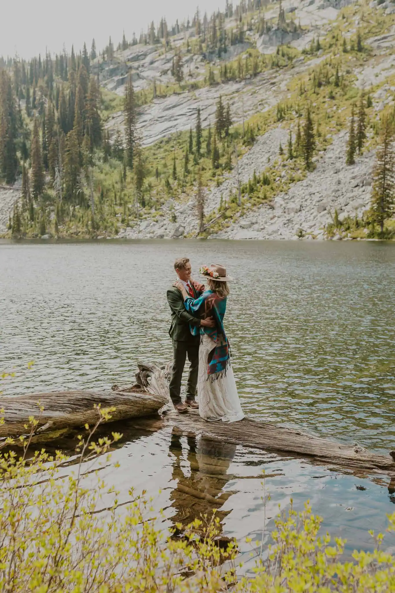 a bride and groom standing on a log in a lake
