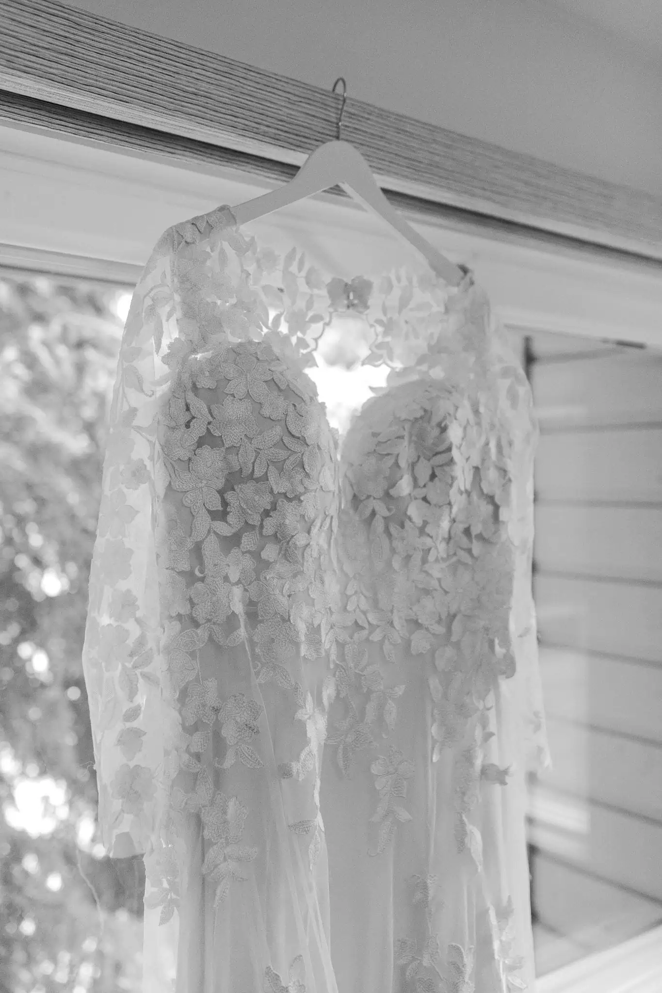 a long sleeved lace wedding dress hanging on a window