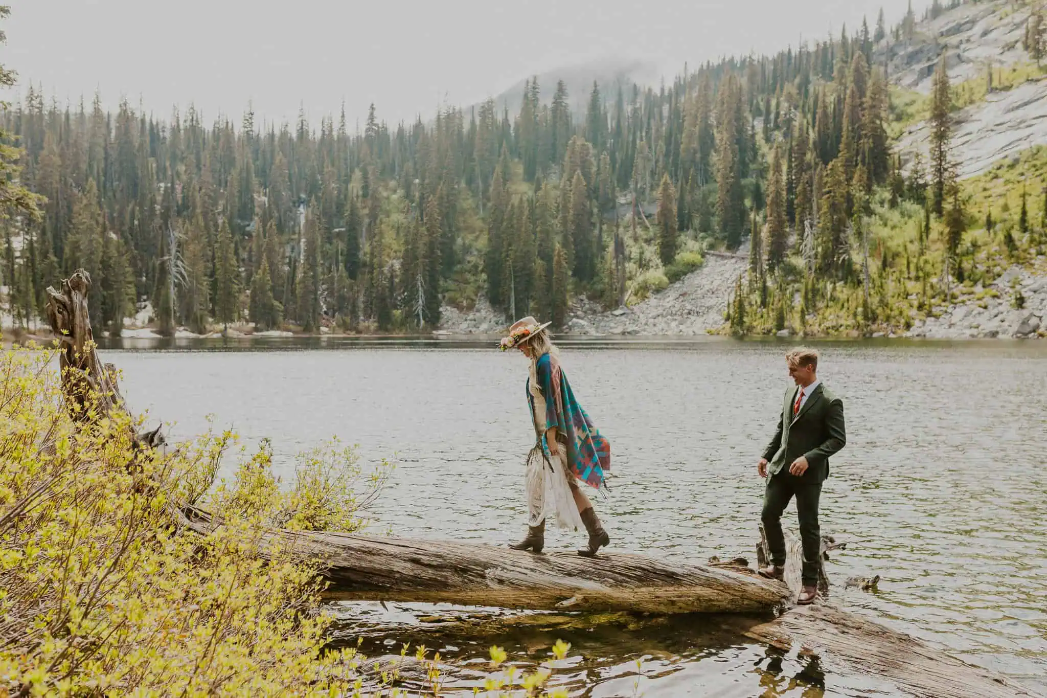 a bride and groom standing on a log in a lake