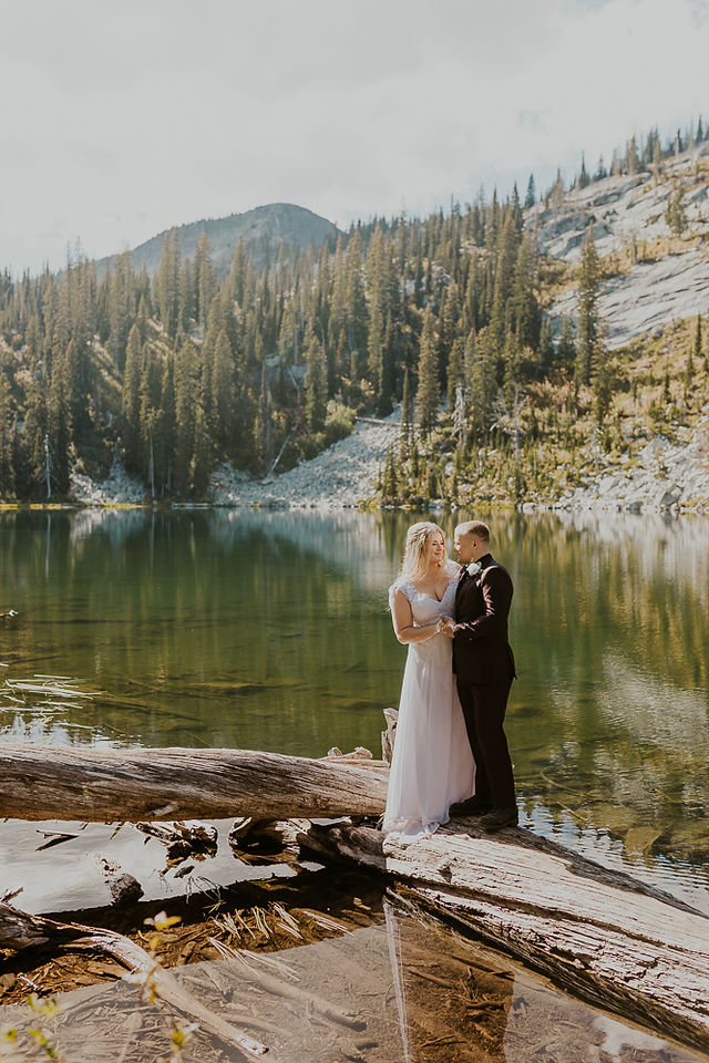 bride and groom walking across a log on a lake
