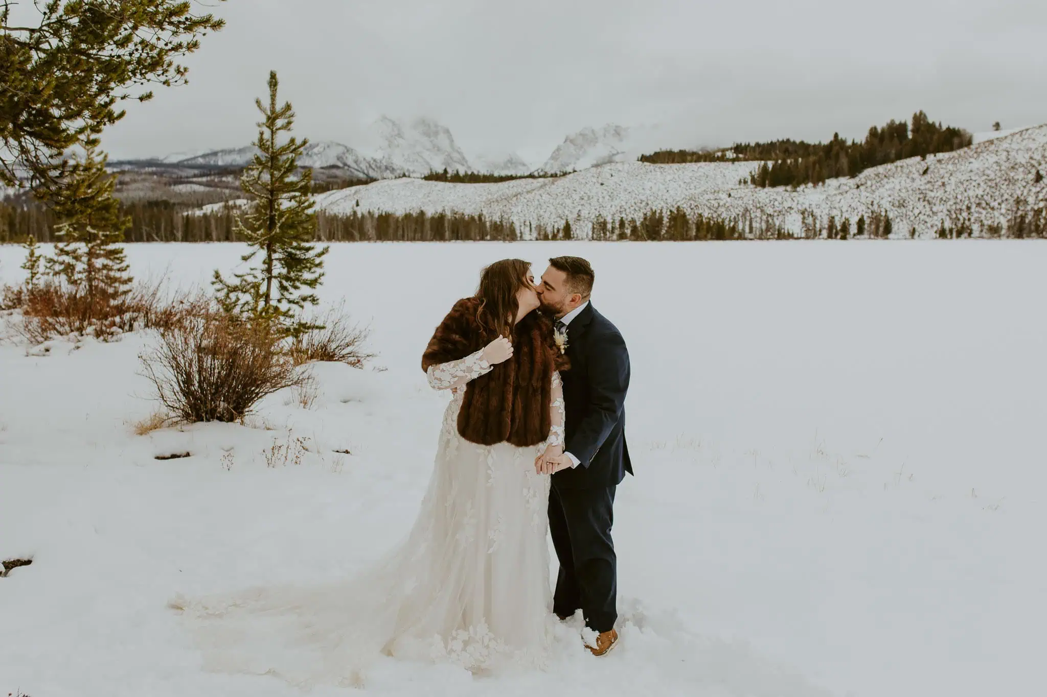 an eloping couple kissing in front of snowy mountains