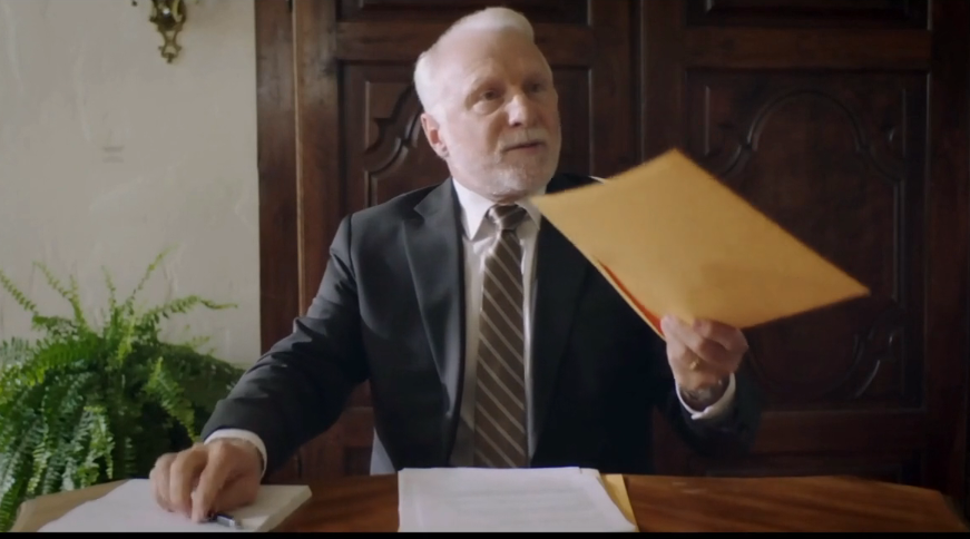 Jean-François Blanchard dans le rôle du notaire Bachand dans la série Nuit Blanche, tend une enveloppe à une personne hors champ.