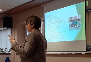 Lady presenting in front of a screen with a slide show