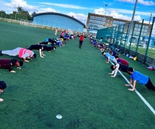 a row of children doing press ups outside as an adult watches