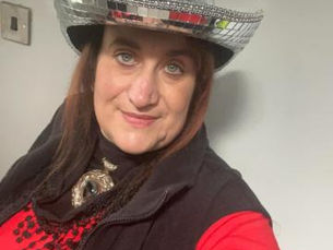 Woman smiling, wearing a shiny disco ball hat, red top, and black vest with "CNDY" text, against a plain gray background.
