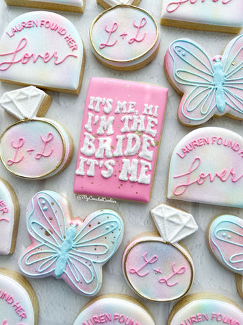 Personalized decorated sugar cookies in soft pink and blue with butterflies, diamond rings, and hand-lettered designs.