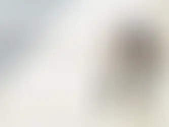 Five people stand in a circle, stacking hands in teamwork, on a bright, tiled floor with natural light. All are smiling.