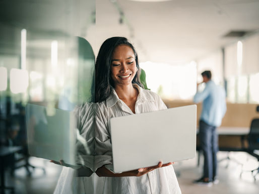 Woman employee leaning on a wall holding a laptop and smiling.