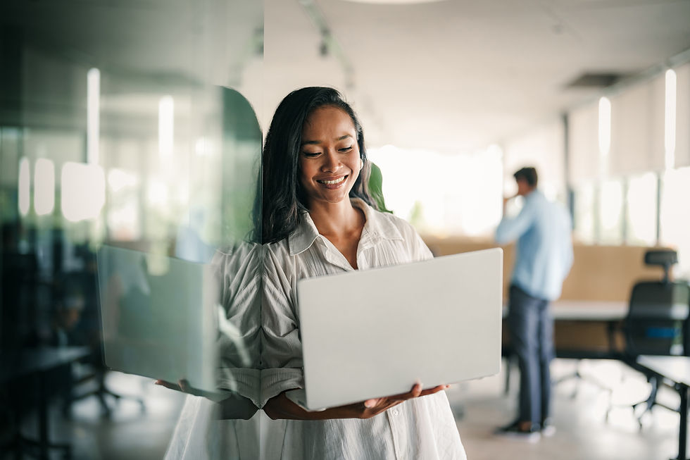 Woman employee leaning on a wall holding her laptop.