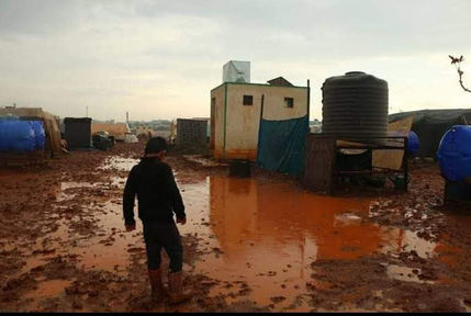 A boy walking through a flooded camp made out of tents