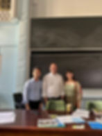 Three people standing behind a desk in front of a blackboard smiling at the camera
