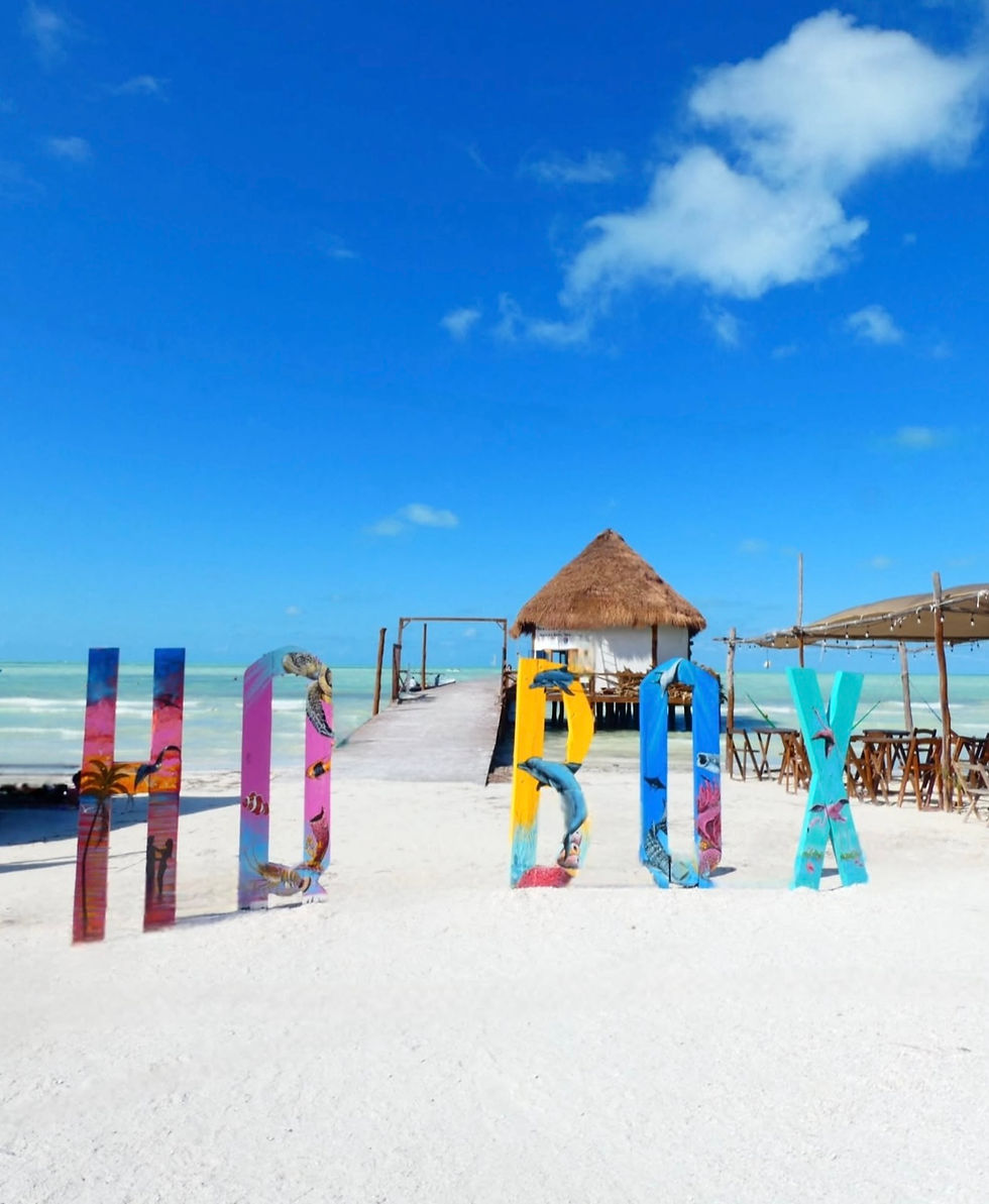 Letras coloridas de “Holbox” frente al mar con cielo despejado.