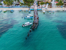 Vista aérea del malecón de Puerto Morelos con el faro inclinado, la playa y el mar Caribe al fondo.