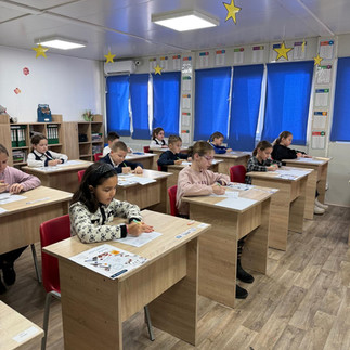 Perspectivă din spatele clasei, surprinzând rândurile de bănci ocupate de elevi în timpul unei activități educaționale.