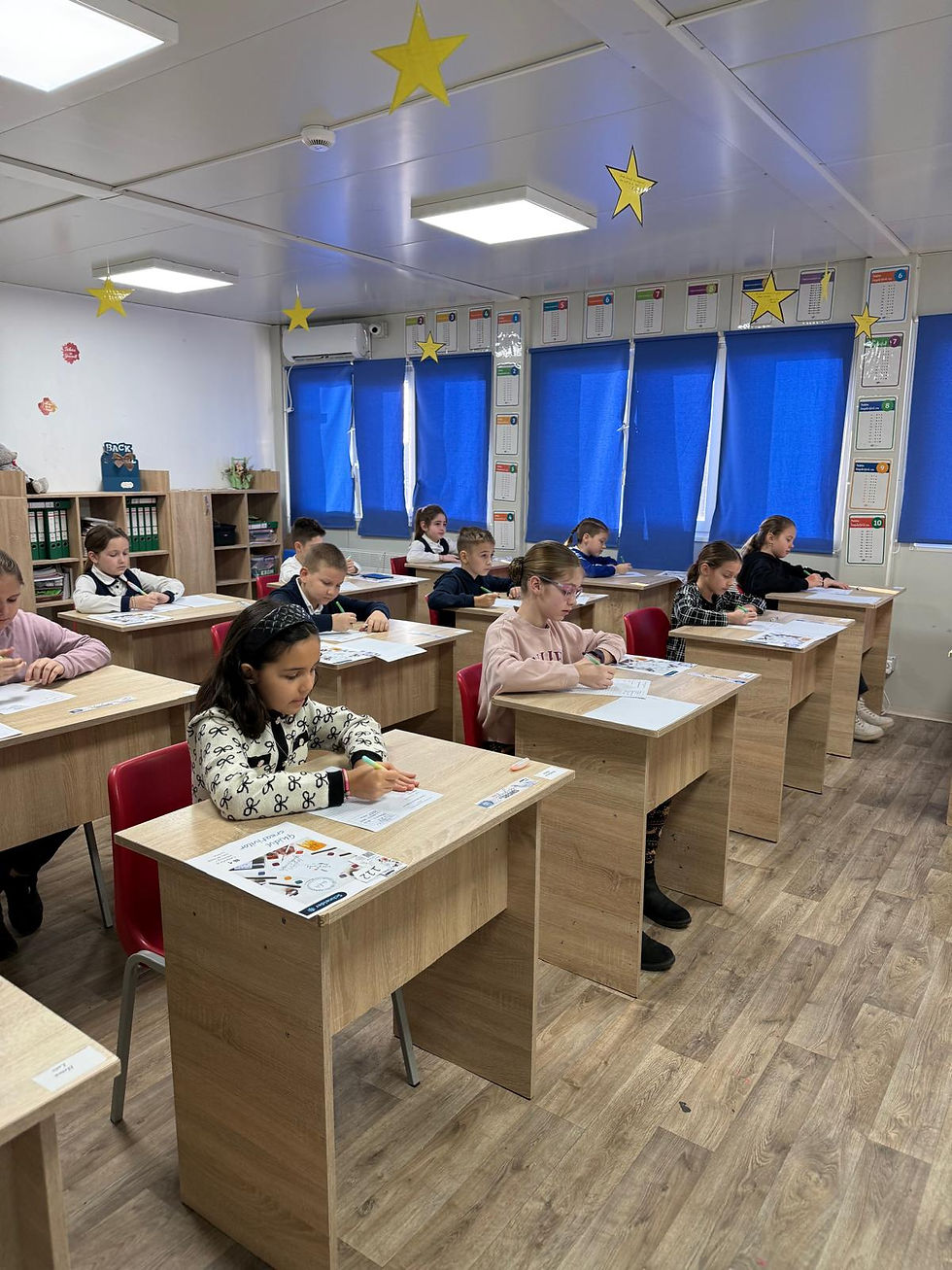 Elev copii concentrându-se pe un test în clasă, cu ferestre albastre, stele galbene pe tavan, bănci din lemn și podea mozaicată.