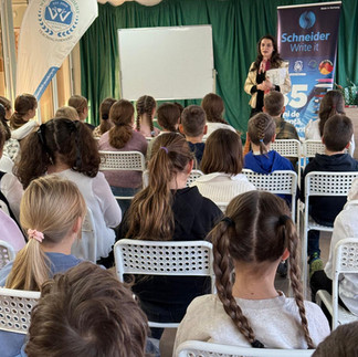 Un grup de elevi văzuți din spate, asistând la o prezentare susținută de o coordonatoare în fața unui ecran de proiecție.