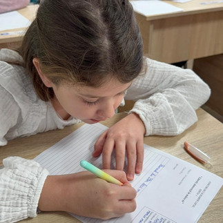 Plan apropiat cu o elevă care scrie cu grijă, folosind un instrument de scris colorat.