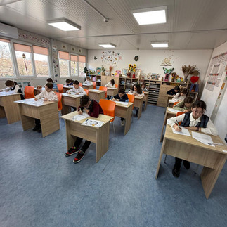 Vedere de ansamblu a unei săli de clasă luminoase, cu elevi așezați individual în bănci, lucrând în liniște.