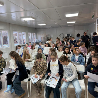 O sală plină de copii așezați pe scaune, participând interactiv la un eveniment sau atelier școlar.