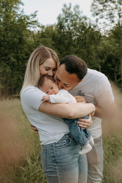 Parents embrassant tendrement leur bébé dans un champ verdoyant et naturel.