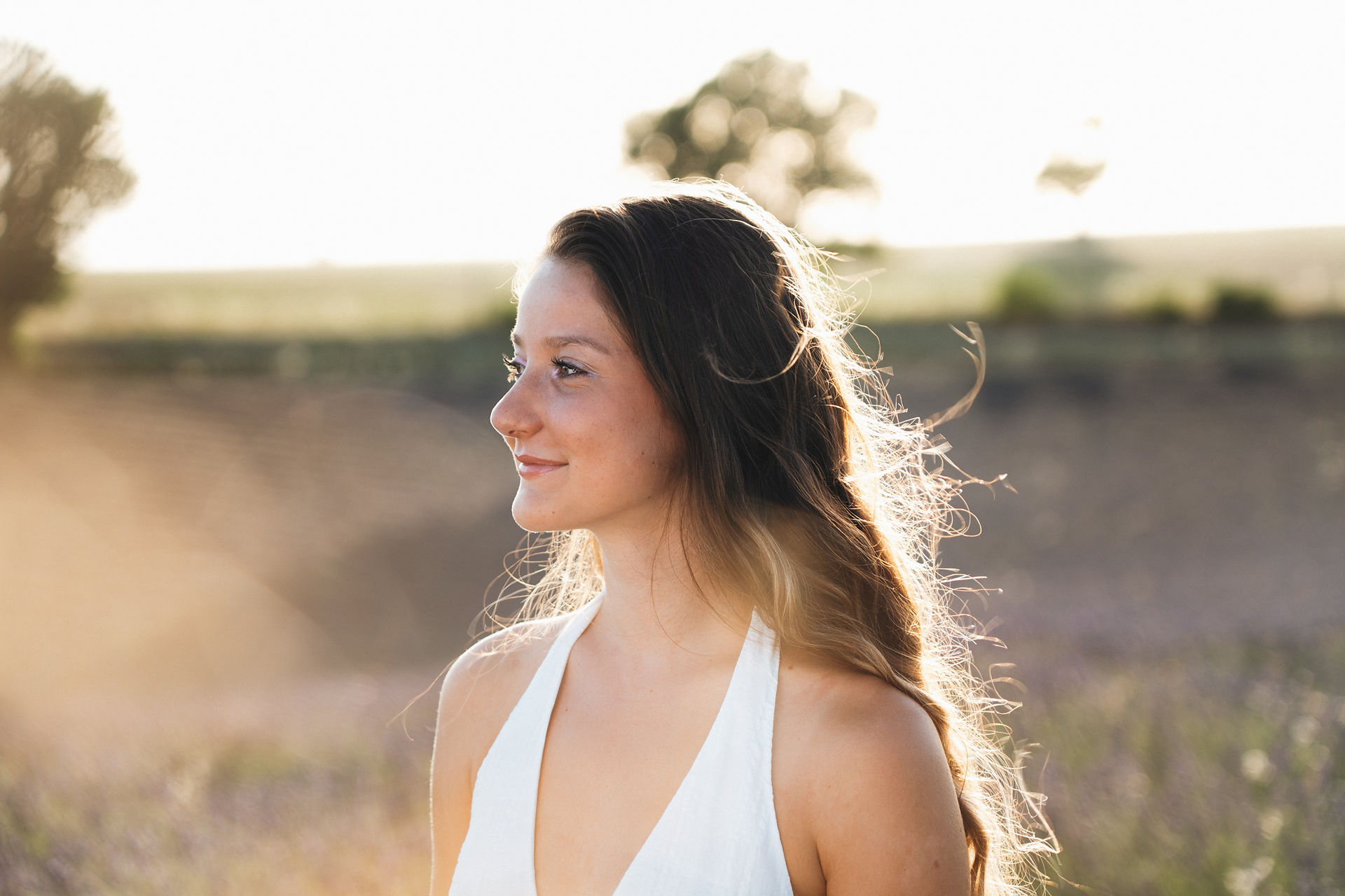 portrait paysage d'une jeune femme au cheveux long dans un champs au coucher de soleil