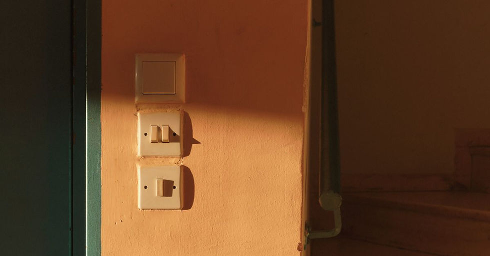 Three light switches on a warm orange wall, lit by natural sunlight, casting soft shadows.