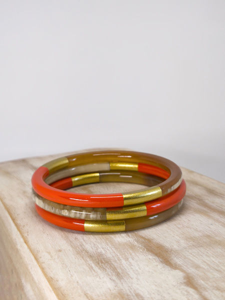 Trois joncs en corne naturelle, brique et doré de 6 mm, présentés sur un support en bois.