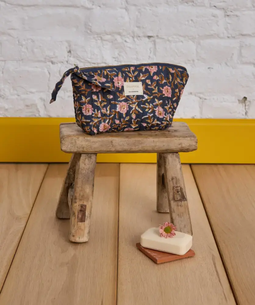 Pochette à maquillage Scarlett Encre posée sur un tabouret en bois rustique avec un savon décoré de fleur en fond