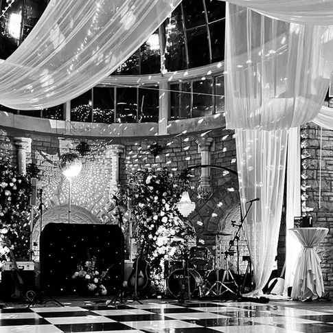 Elegant black-and-white wedding venue with draped fabric and string lights. Musical instruments and floral decor are set against stone walls.