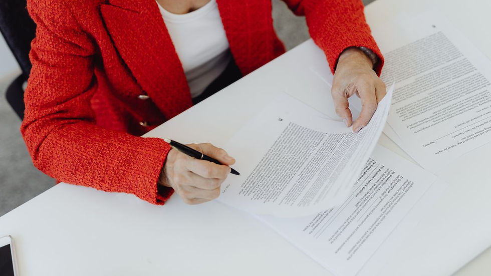 A woman in a red formal coat signing a contract agreement on a white table