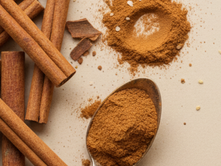 A flat laying spoon with cinnamon next to cinnamon sticks