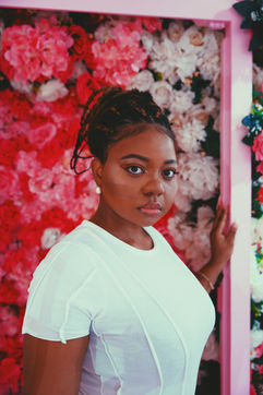 Woman in a white top standing in front of a wall of pink flowers