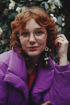 Woman with curly red hair and glasses in a purple puffer jacket outdoors