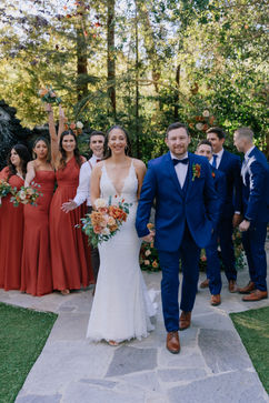 For a fall wedding, the groom and groomsmen will look sharp in classic navy suits, while the bridesmaids will add a pop of color in rust orange dresses. The bride will stand out in a traditional white gown, creating a beautiful contrast against the warm autumn tones.