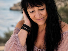 Brigitte Nada-Elisa sitzt nachdenklich am Meer und blickt ruhig nach unten. Das Bild vermittelt Tiefe, Reflexion und innere Ruhe.