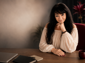 Brigitte Nada-Elisa in heller Chiffonbluse an einem Schreibtisch als Headerbild für einen Blogbeitrag über den Beruf Humanenergetiker und moderne Mentorenstrukturen.