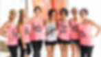 Seven women smiling in pink and white shirts labeled "Wifey," "Brides Maid," and "Maid of Honor" in a bright room with peach dresses.