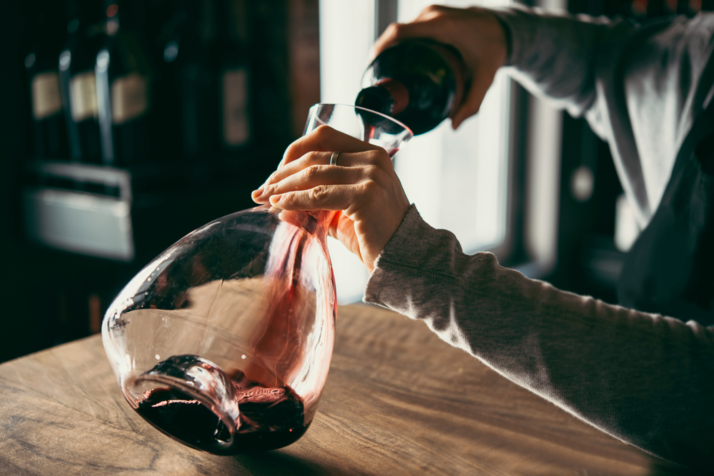 A woman pouring red wine into a glass decanter