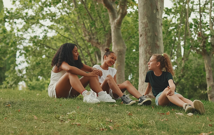 Three girls friends pre-teenage sit on the grass in the park and emotionally talking Three