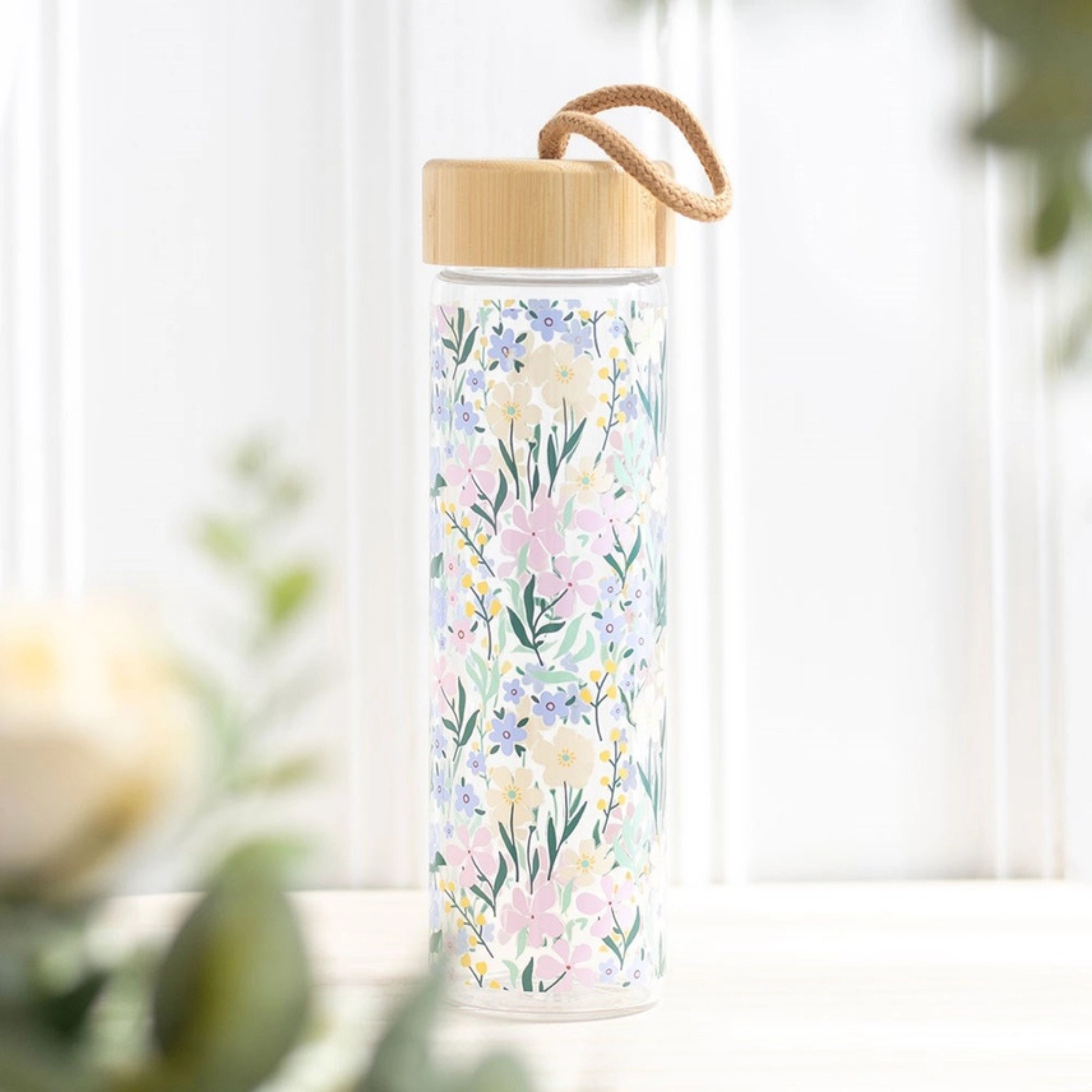 Floral water bottle near soft natural light and greenery