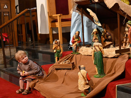 A small child in shepherd costume looks at a nativity scene