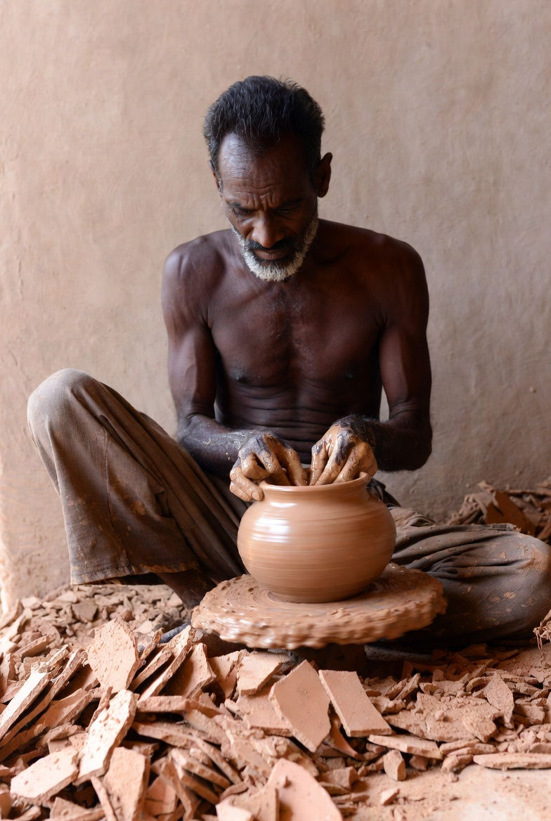 A potter expertly shapes clay on a wheel, surrounded by earthen tones and pottery shards. The mood is focused and serene.