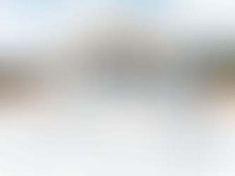 Modern house under construction on a sunny day, with a large blueprint in the foreground and a clear blue sky overhead.