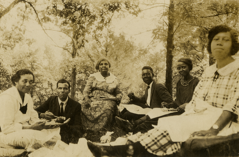 A group of black students, four women and two men, enjoying a picnic in the forest