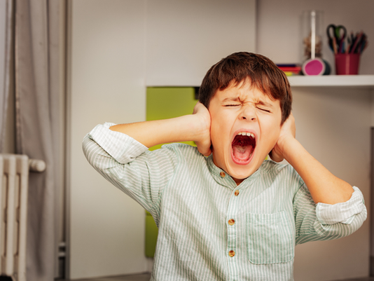 Ein Junge hält sich die Ohren zu und schreit.