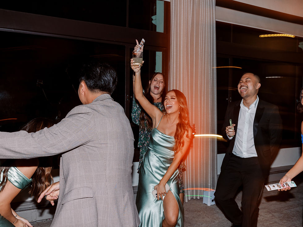 Friends dance and laugh at a nighttime indoor party, one woman in a mint satin dress raising a drink beside a lit column.