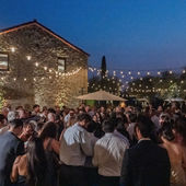 Crowd of dressed-up guests at an outdoor evening party under string lights beside a stone building. A reception of a Napa & Sonoma Winery Wedding.