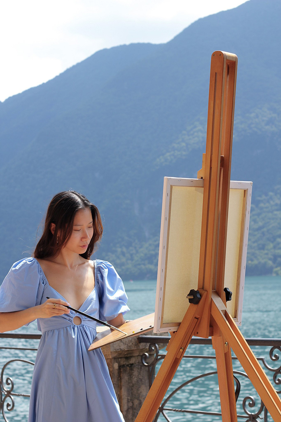 Live painter Linh behind easel, outdoor setting with mountain in the background, blue colours
