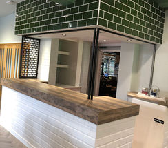 Custom-built champagne bar with bottle green modern tiles and a hardwood bar top in sports venue, by SB Carpentry & Building