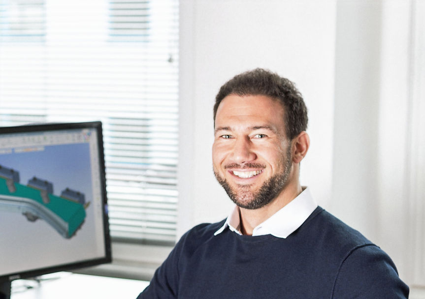 Ingenieur im Werkzeugbau lächelt vor CAD-Bildschirm.